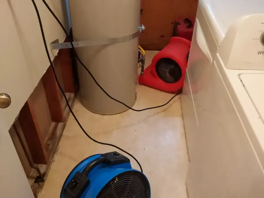 Air movers aimed at an opened wall behind a washer in a laundry area