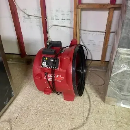 Chanhassen structural drying: a red air mover at an opened lower wall behind plastic sheeting