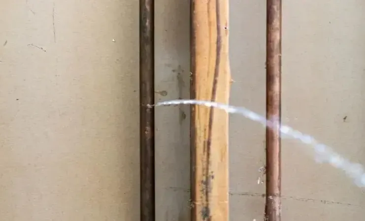 A thin jet of water spraying from a pinhole in a copper pipe inside an opened wall