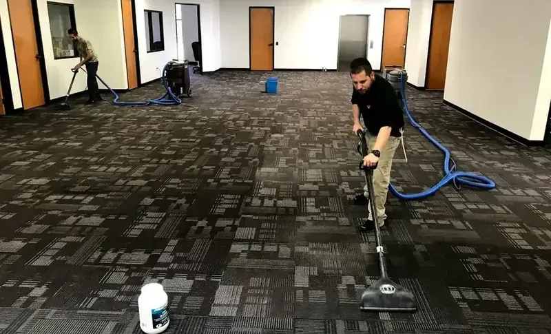 Technicians extracting water from carpet tile in an office space