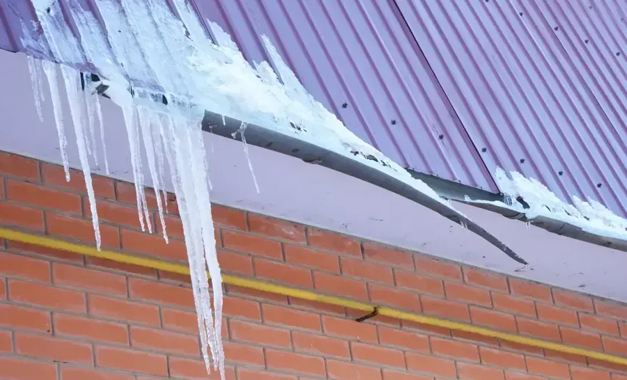 A ridge of ice and long icicles along a roof edge above a brick wall