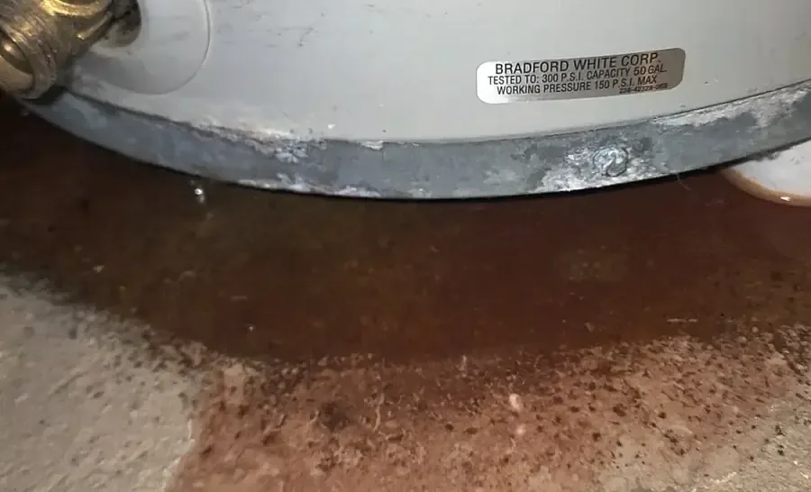 Rust-colored water pooled on concrete around the base of a leaking water heater
